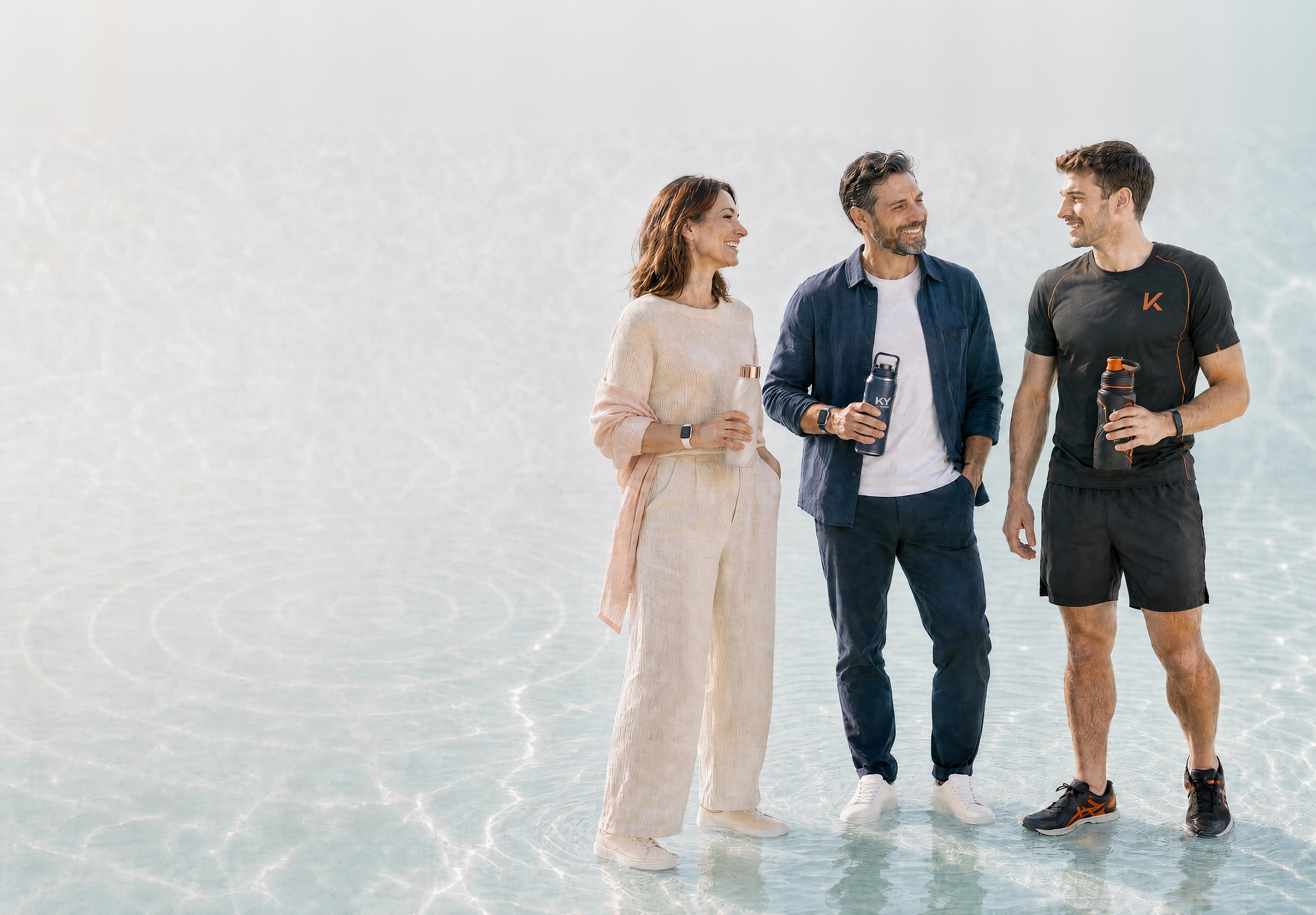 A woman, a man and an athlete standing together in shallow, sunlit water